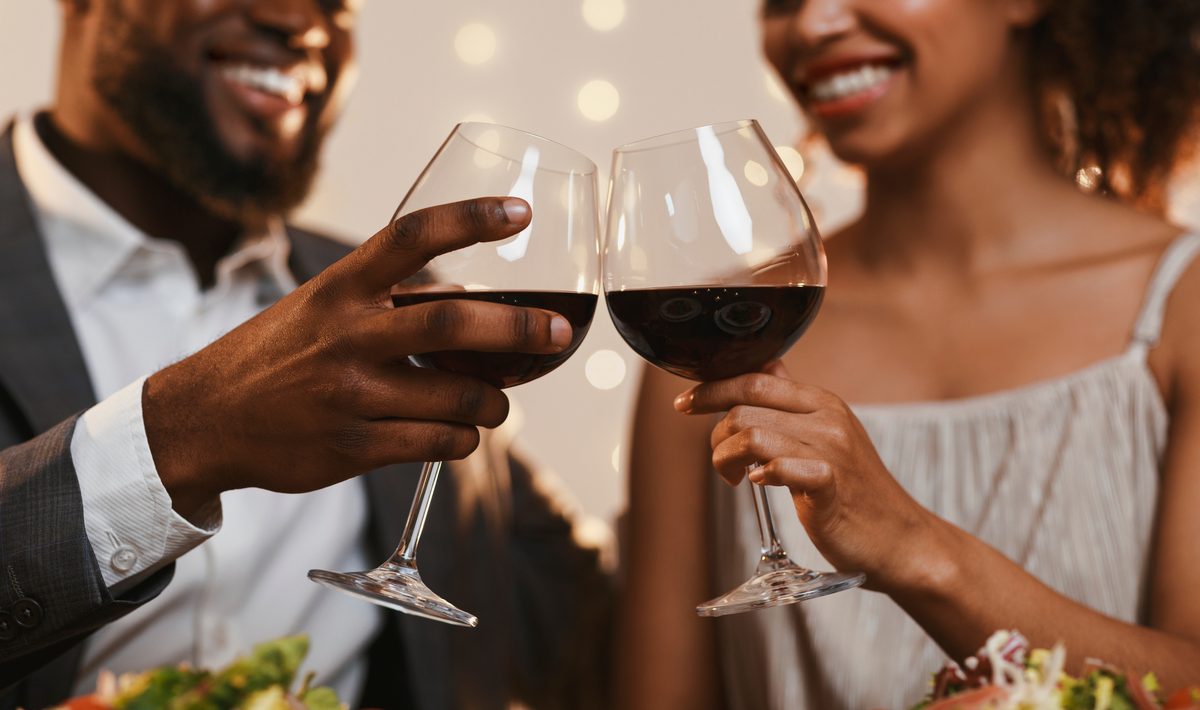 A Black couple toasting with red wine on a candlelit first date, The Broom List