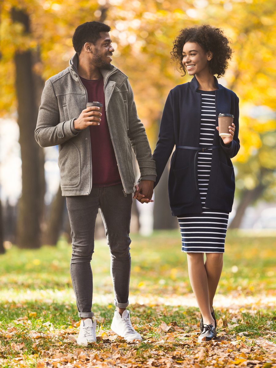 A Black couple holding hands with coffee on an autumn first-date walk