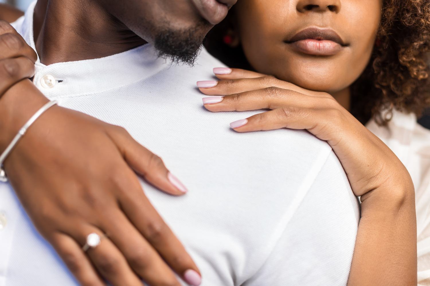 An engaged Black couple embracing, her engagement ring catching the light