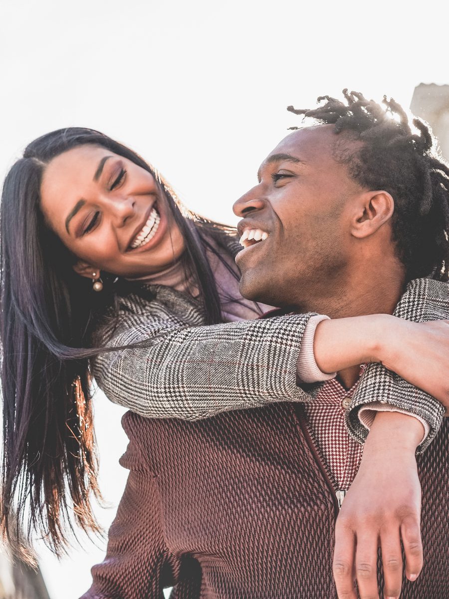A laughing Black couple piggybacking, falling in love